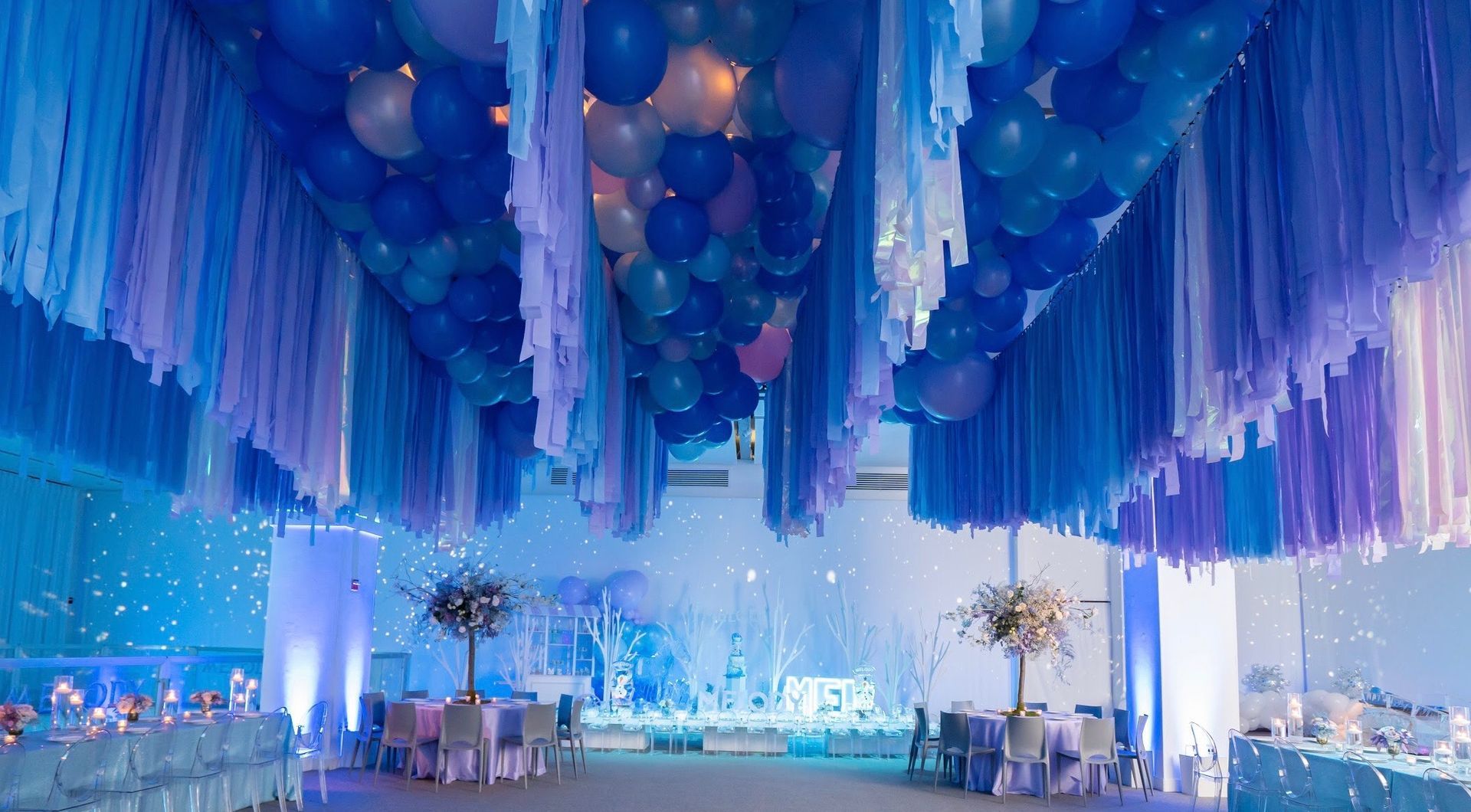 A room with tables and chairs and balloons hanging from the ceiling.