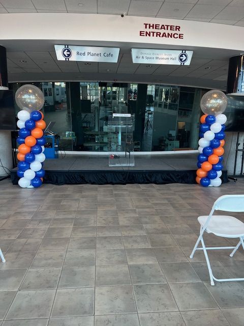 A room with tables and chairs and red flowers and black balloons on the ceiling.