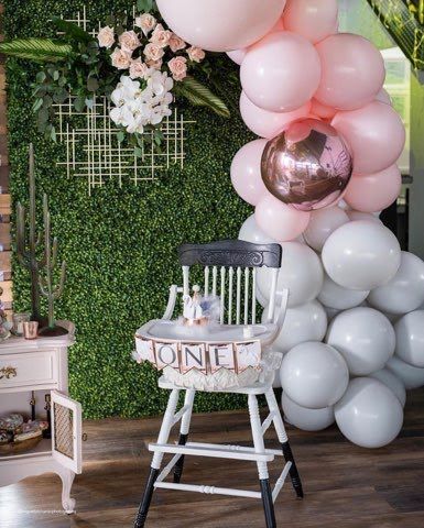 A high chair is sitting in front of a wall of pink and white balloons.