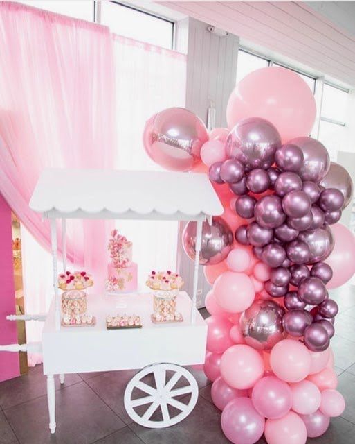 A candy cart is decorated with pink and purple balloons.