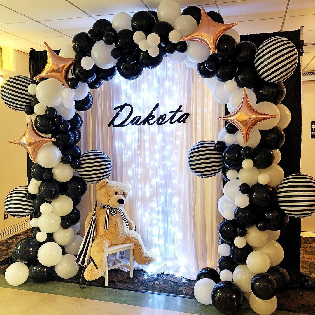 A black and white balloon arch with a teddy bear in front of it.