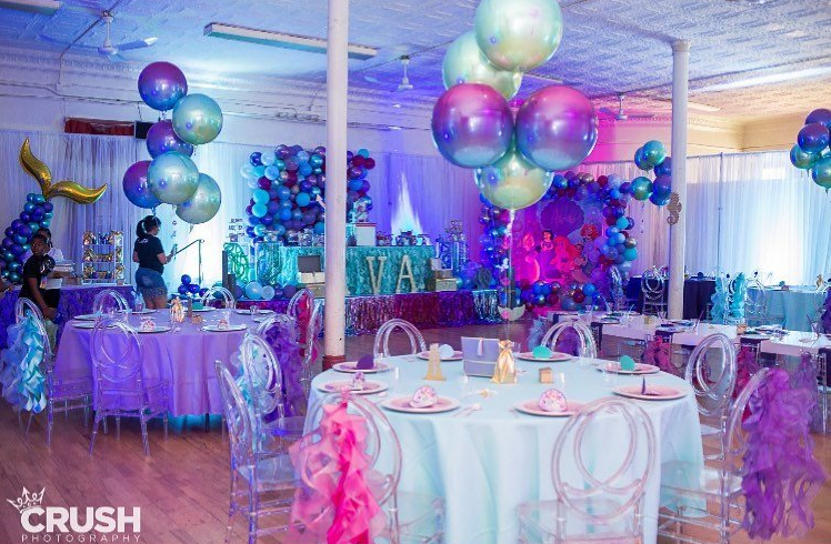 A room filled with tables and chairs decorated for a mermaid themed birthday party.