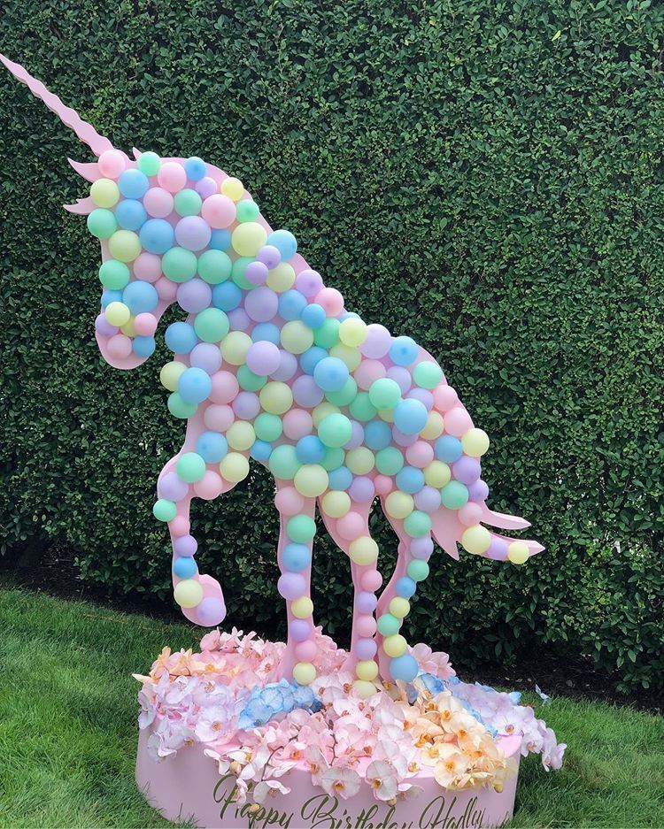 A statue of a unicorn made of balloons is sitting in the grass.