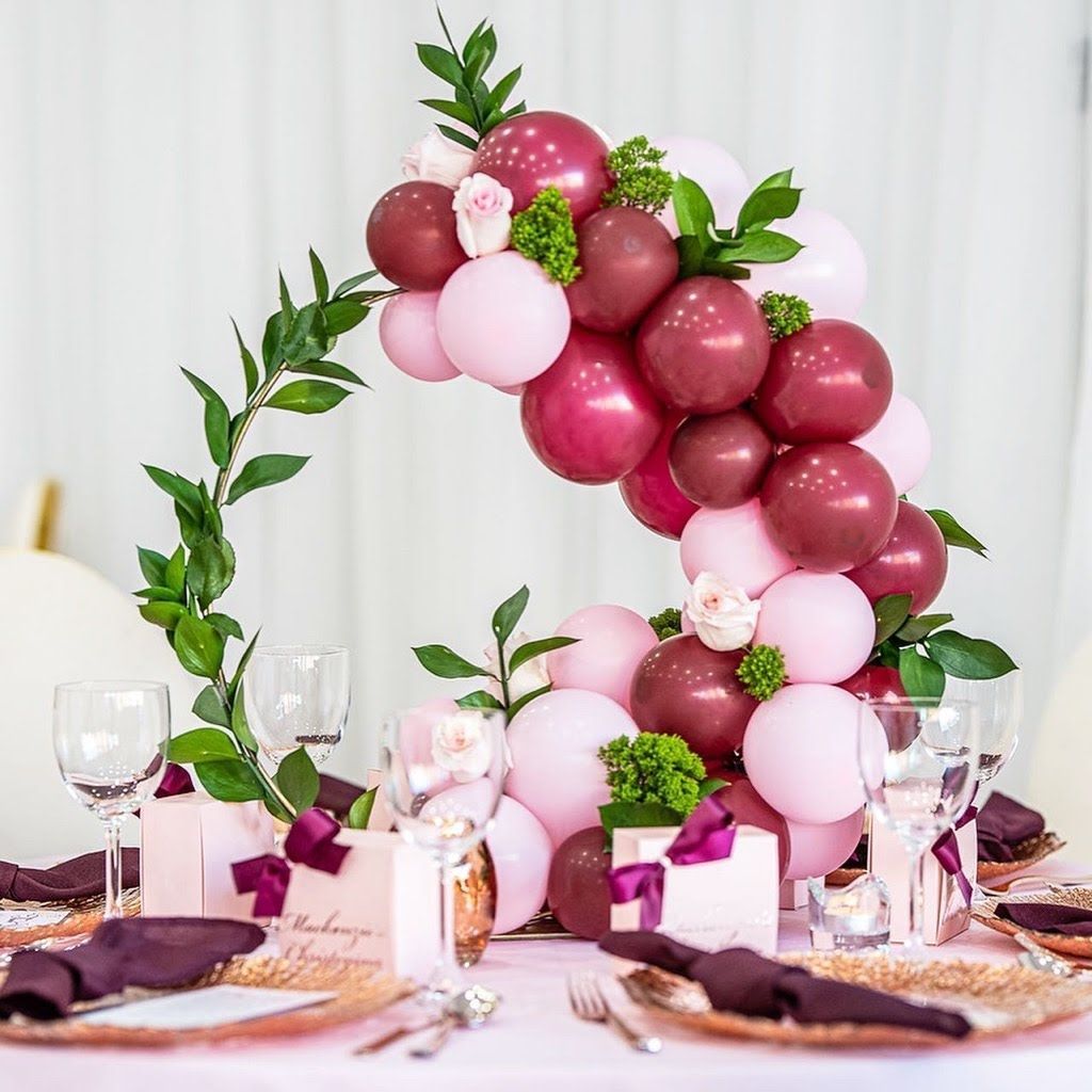 A table decorated with pink and maroon balloons and flowers.