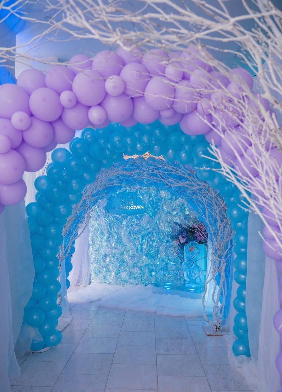 A hallway filled with purple and blue balloons and branches.