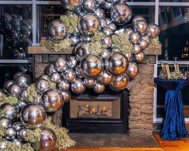 A fireplace decorated with silver balloons and flowers.