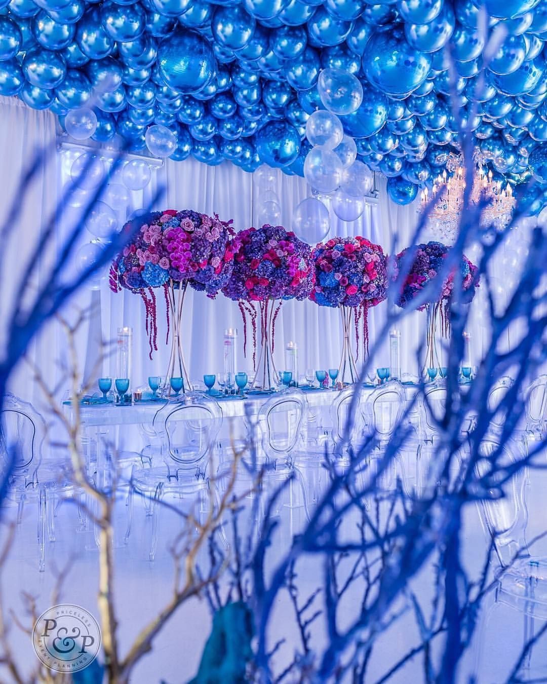A room with blue balloons hanging from the ceiling and flowers in vases.