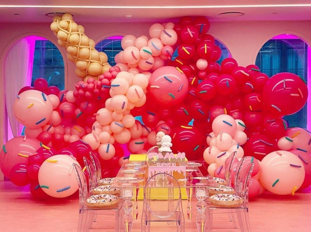 A table and chairs are decorated with pink balloons and sprinkles.