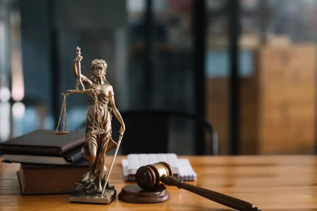 Statue of Lady Justice with scales, books, and gavel on a wooden desk.