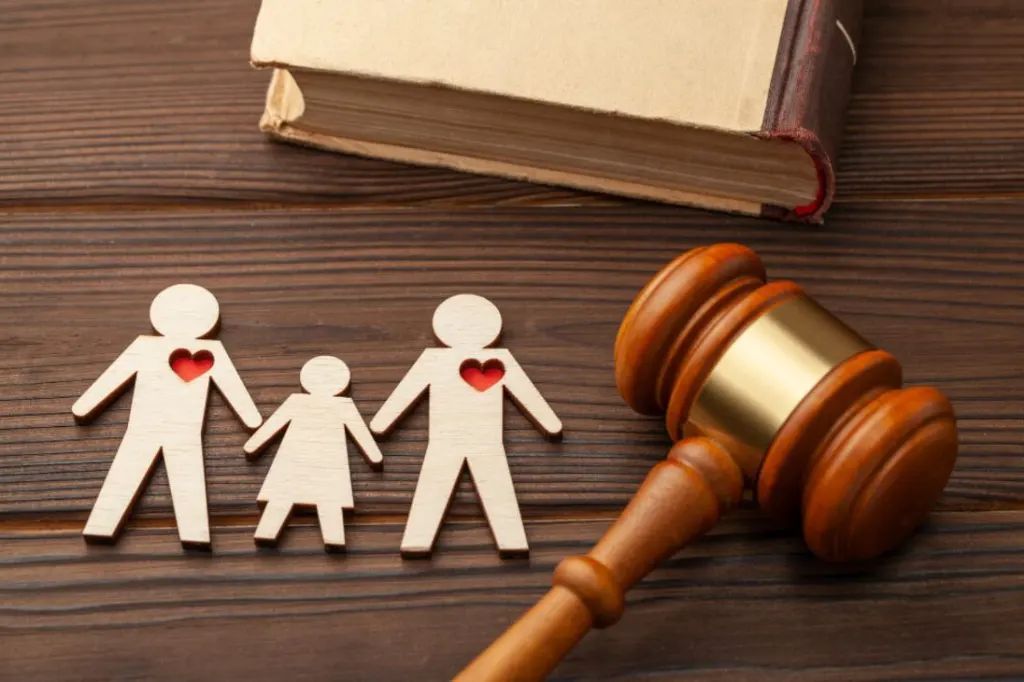 Wooden family cutouts with heart-shaped openings, gavel, and law book on a wood table.