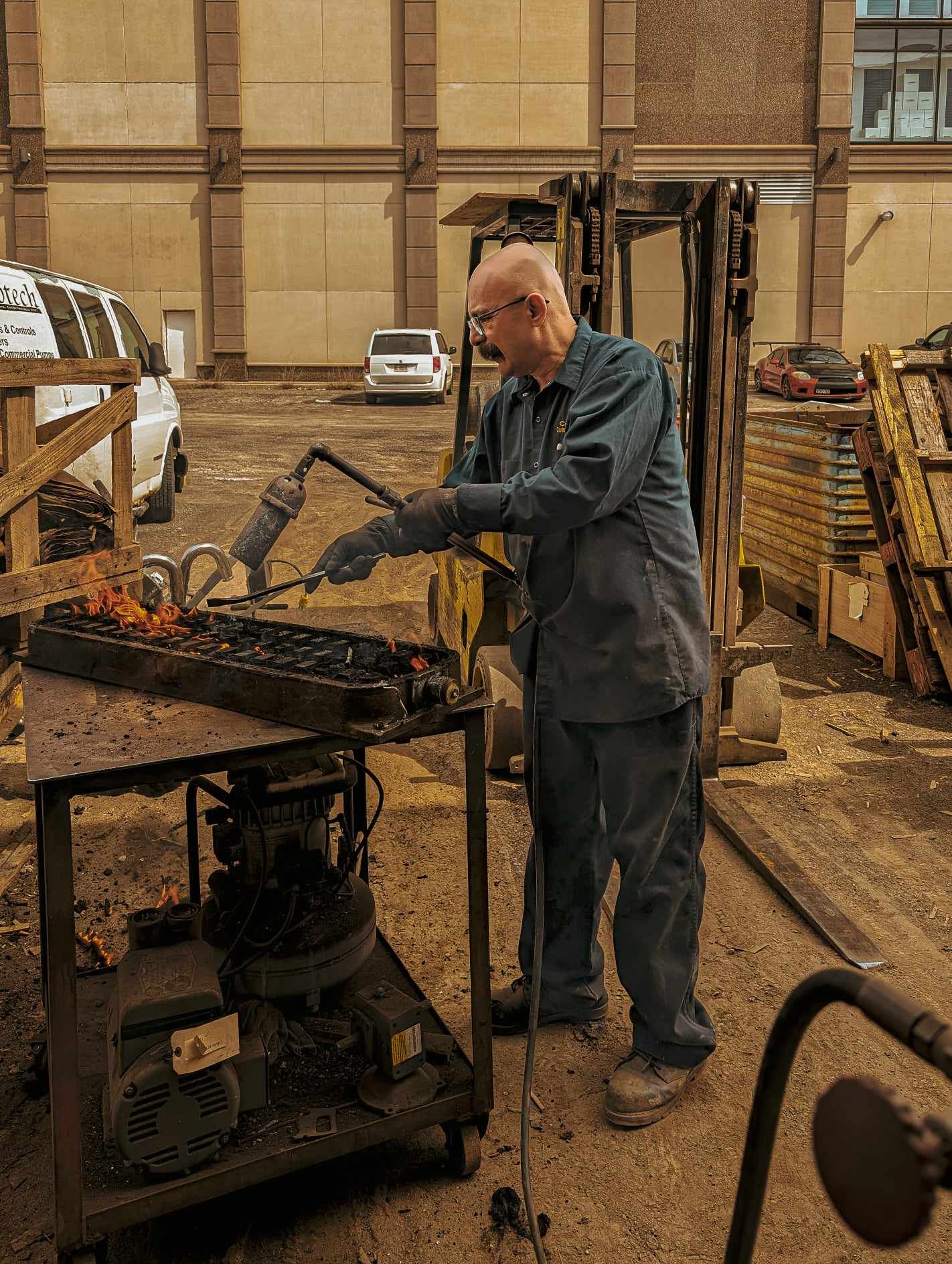 A man is working on a piece of metal in a parking lot.