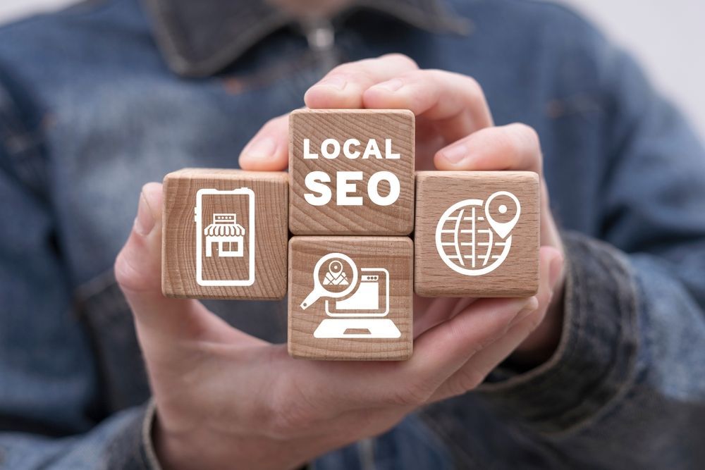 A person is holding wooden blocks with icons on them that say local seo.