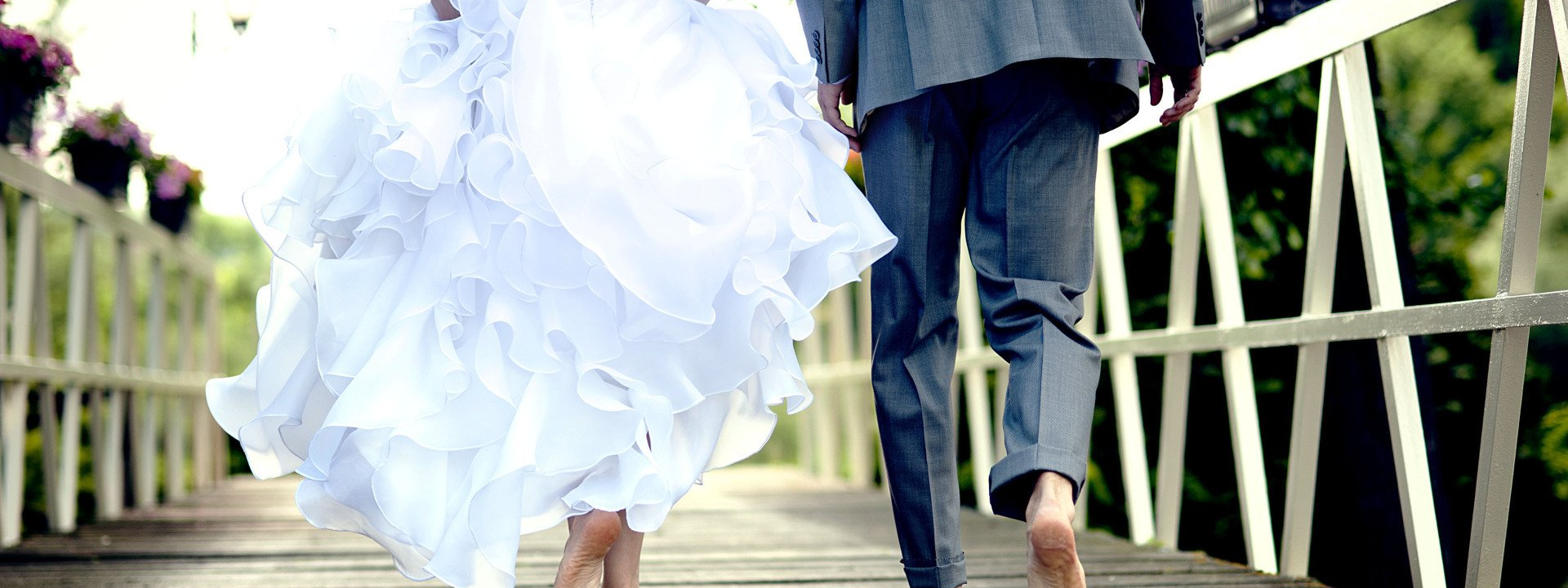 newlyweds walking barefoot across a bridge