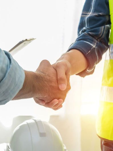 A man and a woman are shaking hands in front of a hard hat.