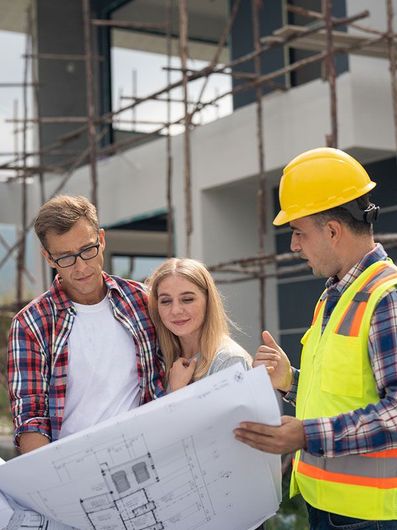 A man and a woman are looking at a blueprint at a construction site.