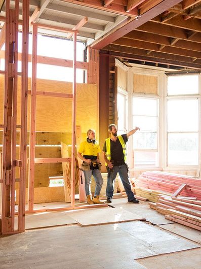 Two construction workers are standing in a room under construction.