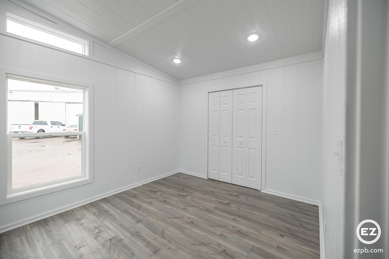 An empty room with hardwood floors , white walls , and a window.