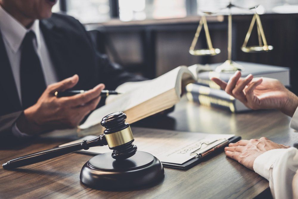 Lawyers consulting at a desk with a gavel, law books, and scales of justice in the background.