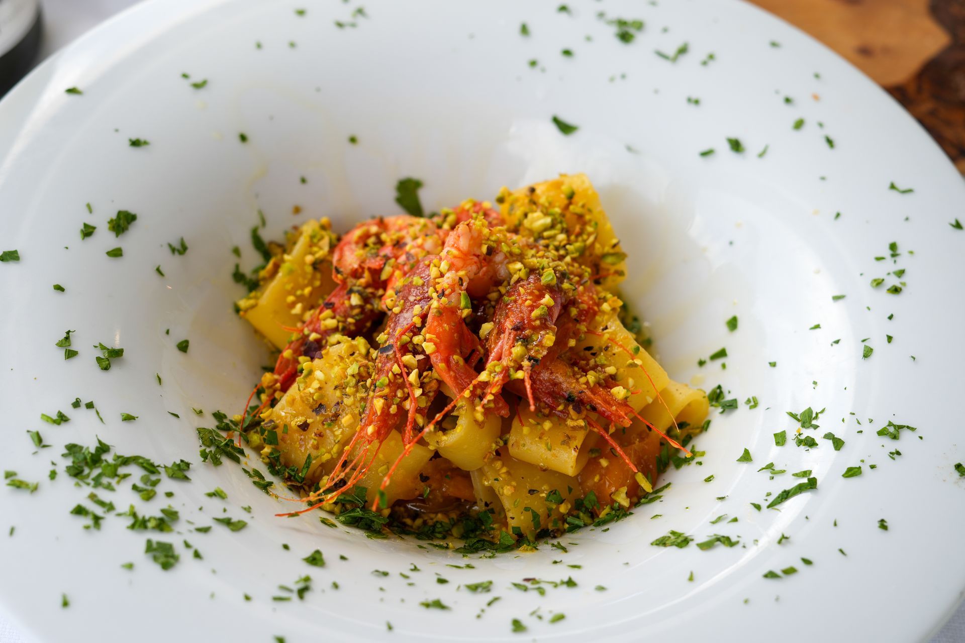 Piatto di pasta con gamberi, salsa di pomodoro e pistacchi in una ciotola bianca, guarnito con prezzemolo.