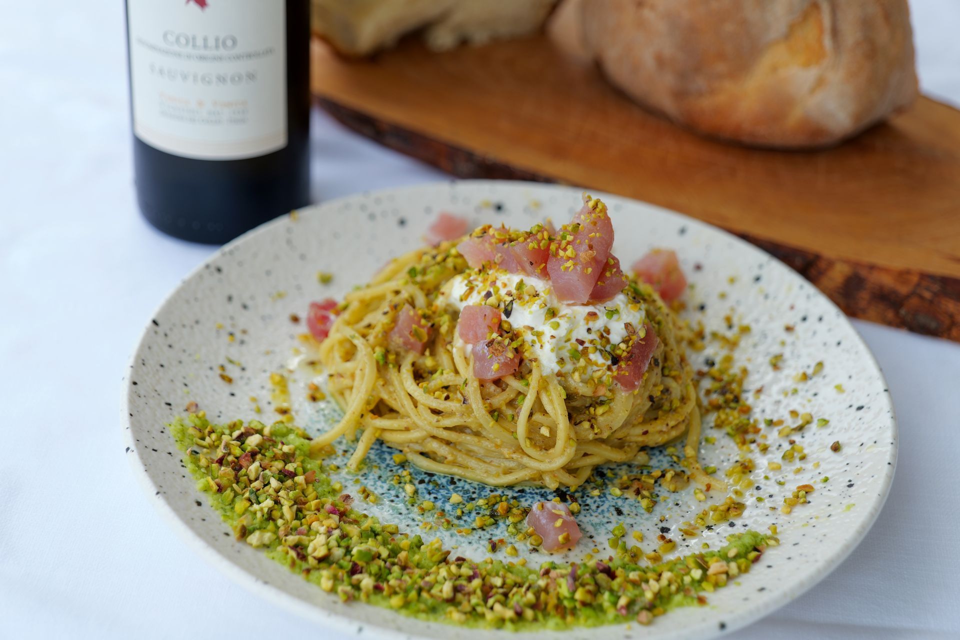 Spaghetti con pistacchi, formaggio e prosciutto. Serviti su un piatto decorato con pane e bottiglia di vino.