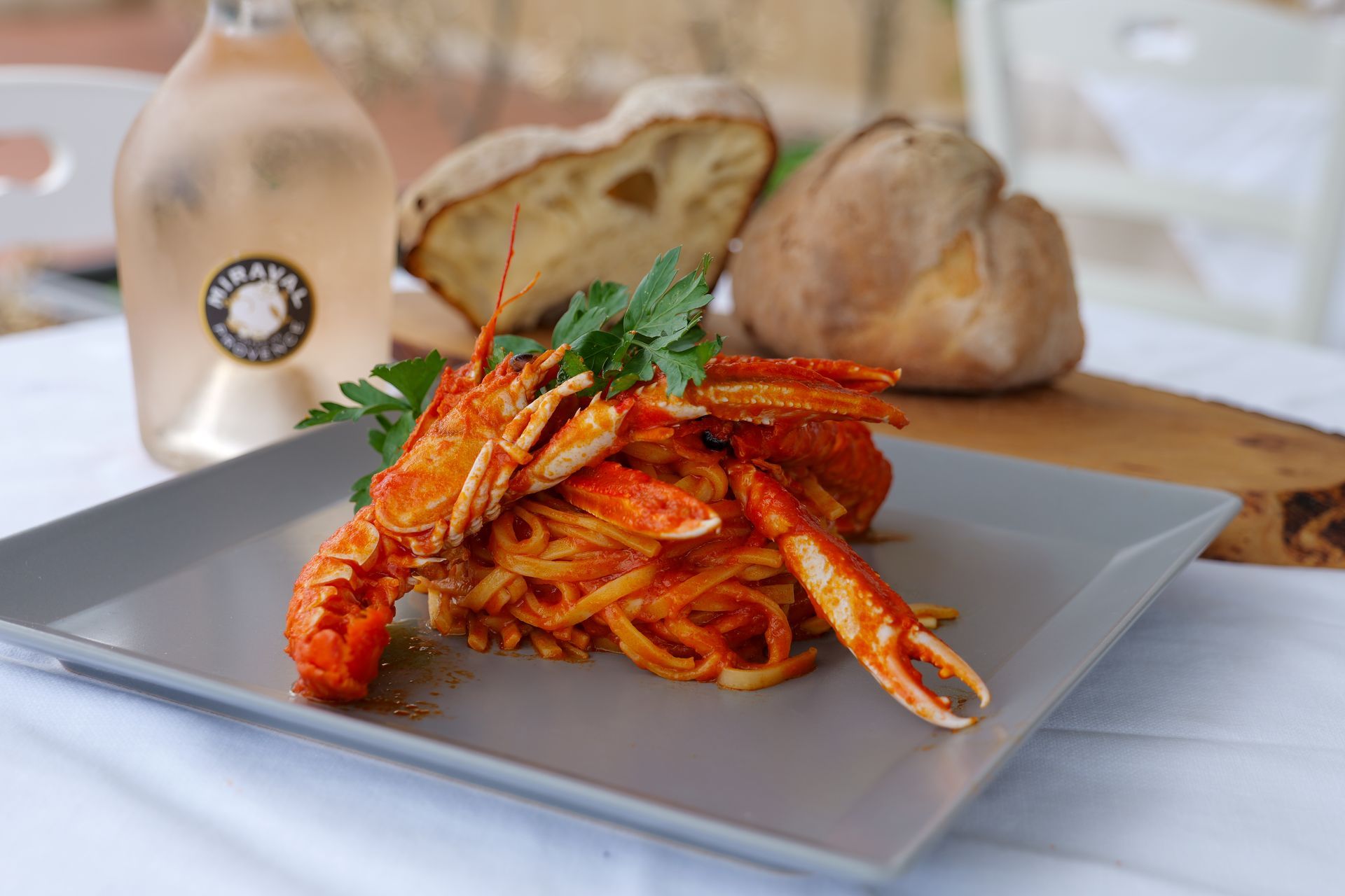 Spaghetti all'astice su un piatto grigio, vino rosato e pane su un tagliere di legno.