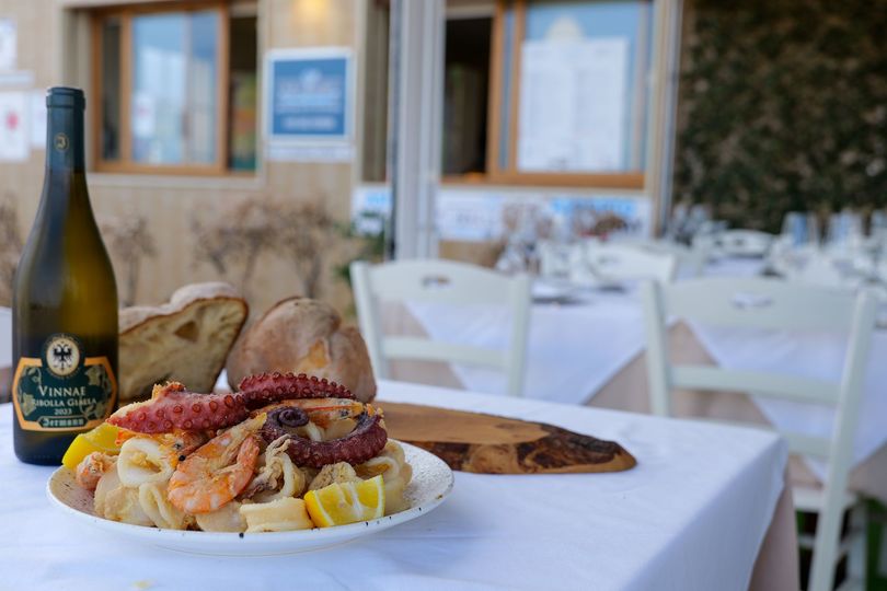Piatto di frutti di mare con vino e pane su un tavolo apparecchiato con tovaglie bianche all'esterno di un ristorante.