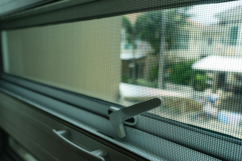Close Up of A Window Screen with A Latch Looking out To a Sunlit Patio and Greenery — Fineworx Joinery in Warnervale, NSW
