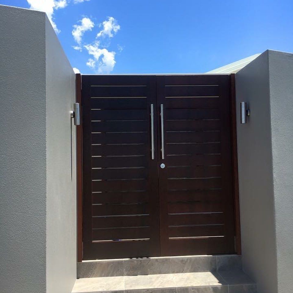 Dark Wooden Double Gate Between Grey Walls Under a Blue Sky with Clouds — Fineworx Joinery in Newcastle, NSW