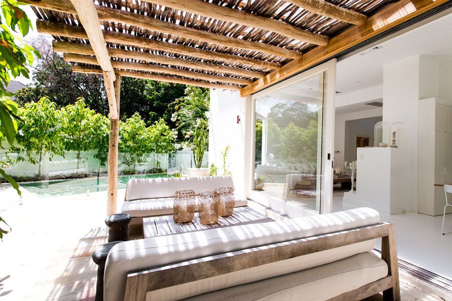 Open-air patio with striped sofa, dining table, and wooden pergola beside a bright pool and garden — Fineworx Joinery in Warnervale, NSW