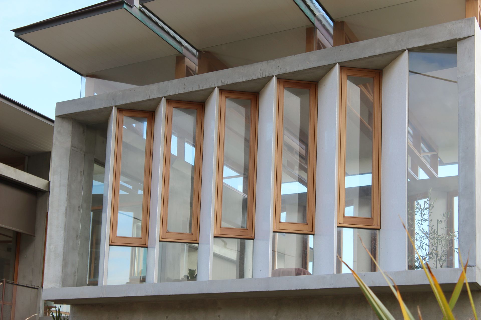Modern building facade with tall wooden-framed windows and white walls under a concrete overhang — Fineworx Joinery in Warnervale, NSW