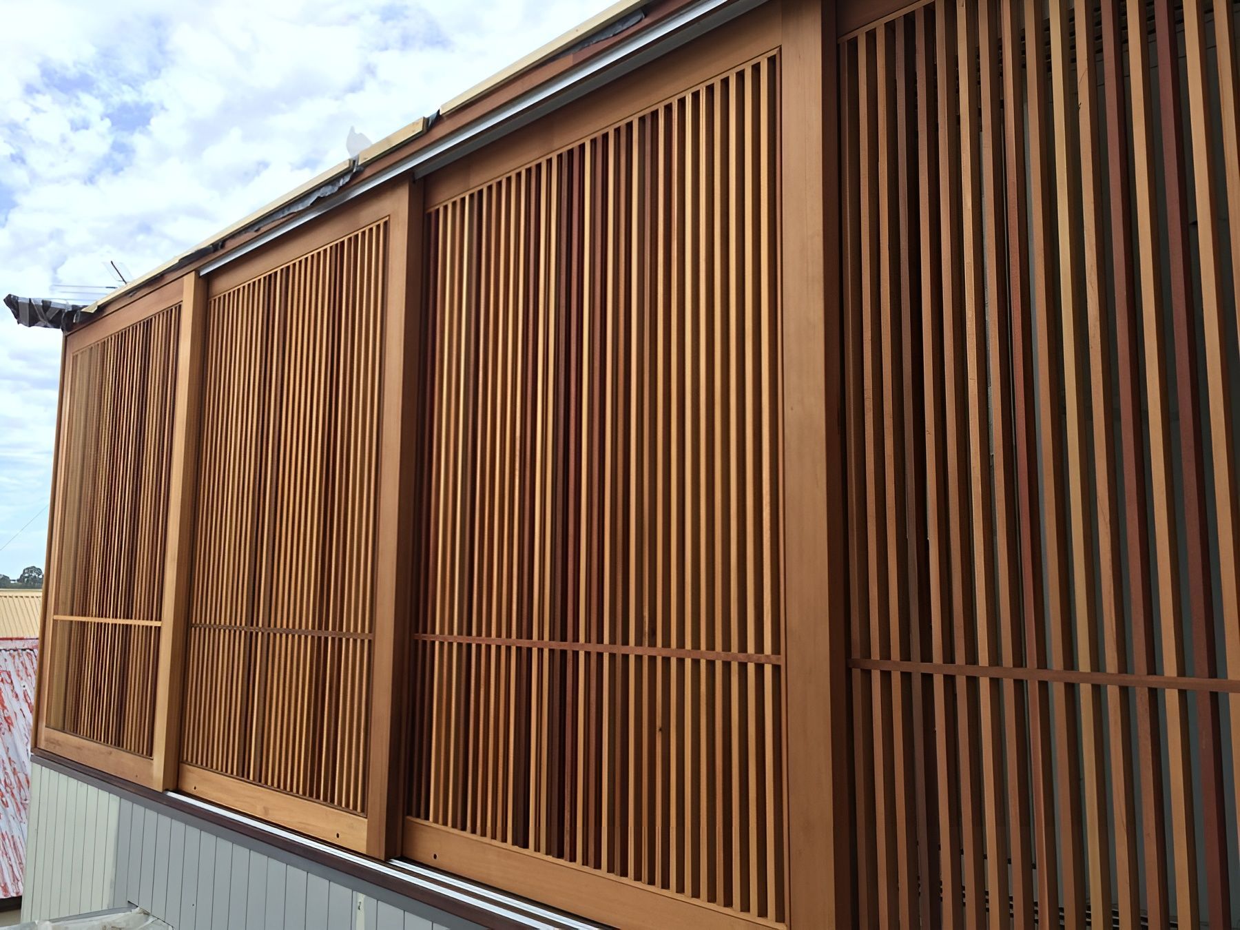 Rust Coloured Slatted Metal Fence Along a Sidewalk Under a Partly Cloudy Sky — Fineworx Joinery in Warnervale, NSW