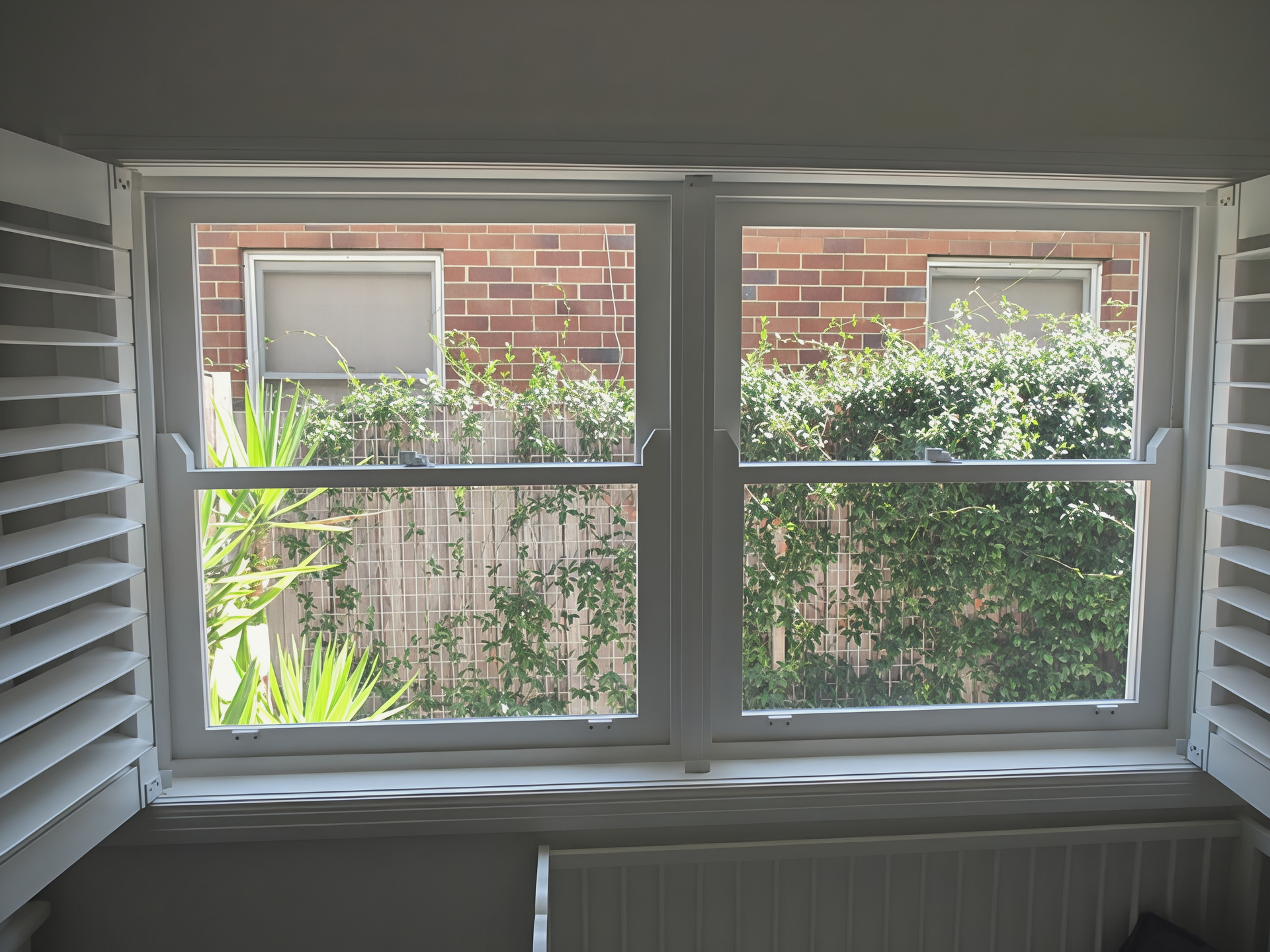 White Window Shutters Framing a View of A Brick Building and Green Bushes Outside — Fineworx Joinery in Hunter Valley, NSW