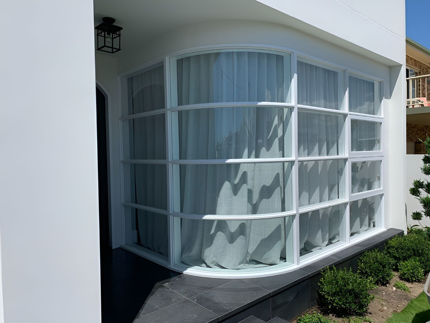 Curved Glass Window with White Curtains on A White Building Exterior — Fineworx Joinery in Warnervale, NSW