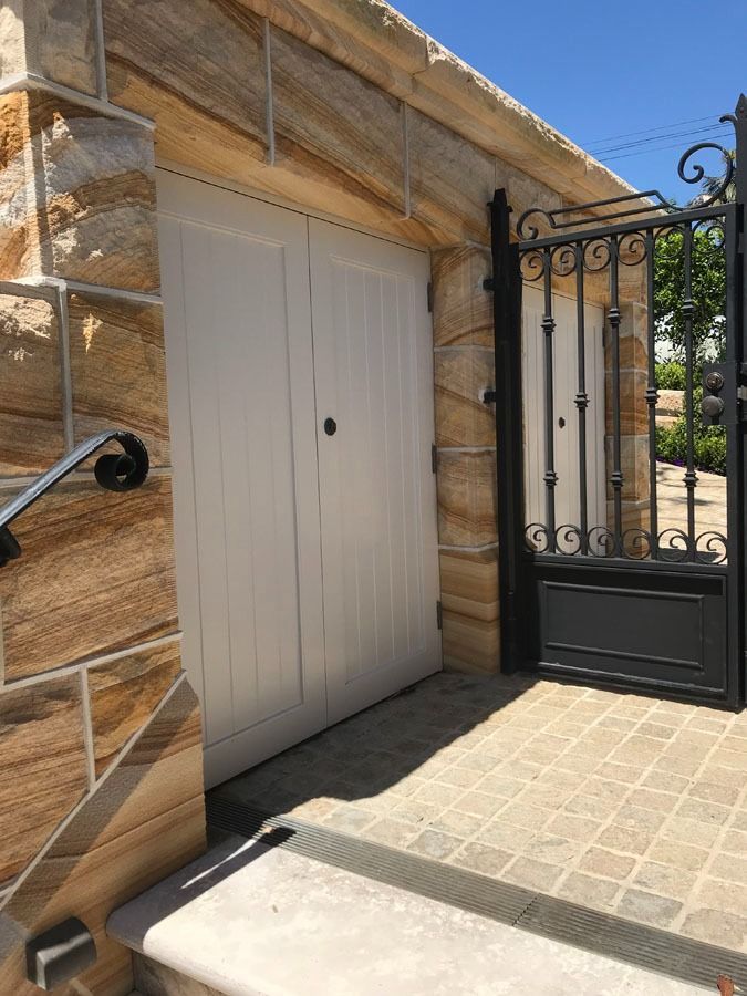White Garage Door Beside Black Iron Gate and Stone Wall in A Sunlit Driveway — Fineworx Joinery in Warnervale, NSW