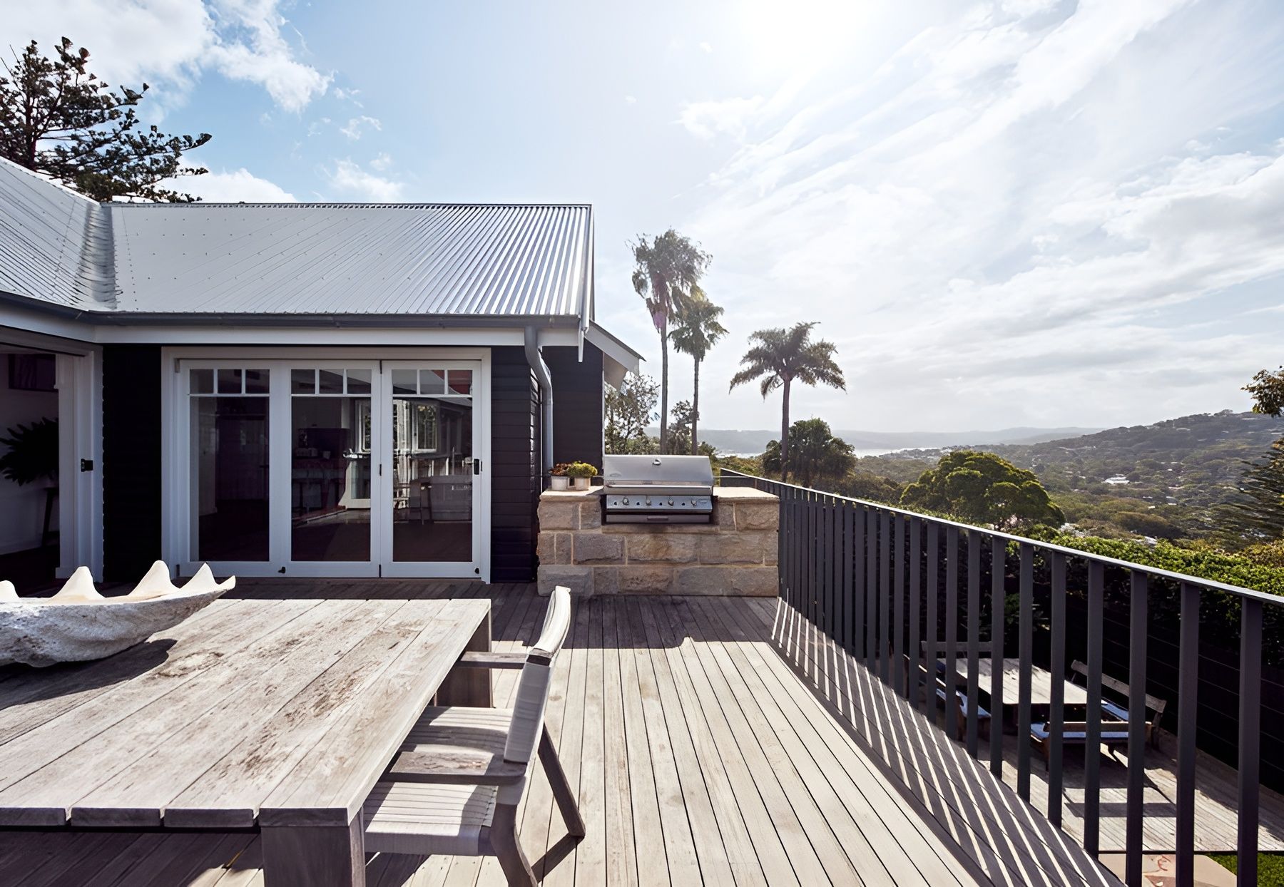 Wooden deck with table and chairs beside a modern house, overlooking a sunny hillside view — Fineworx Joinery in Warnervale, NSW