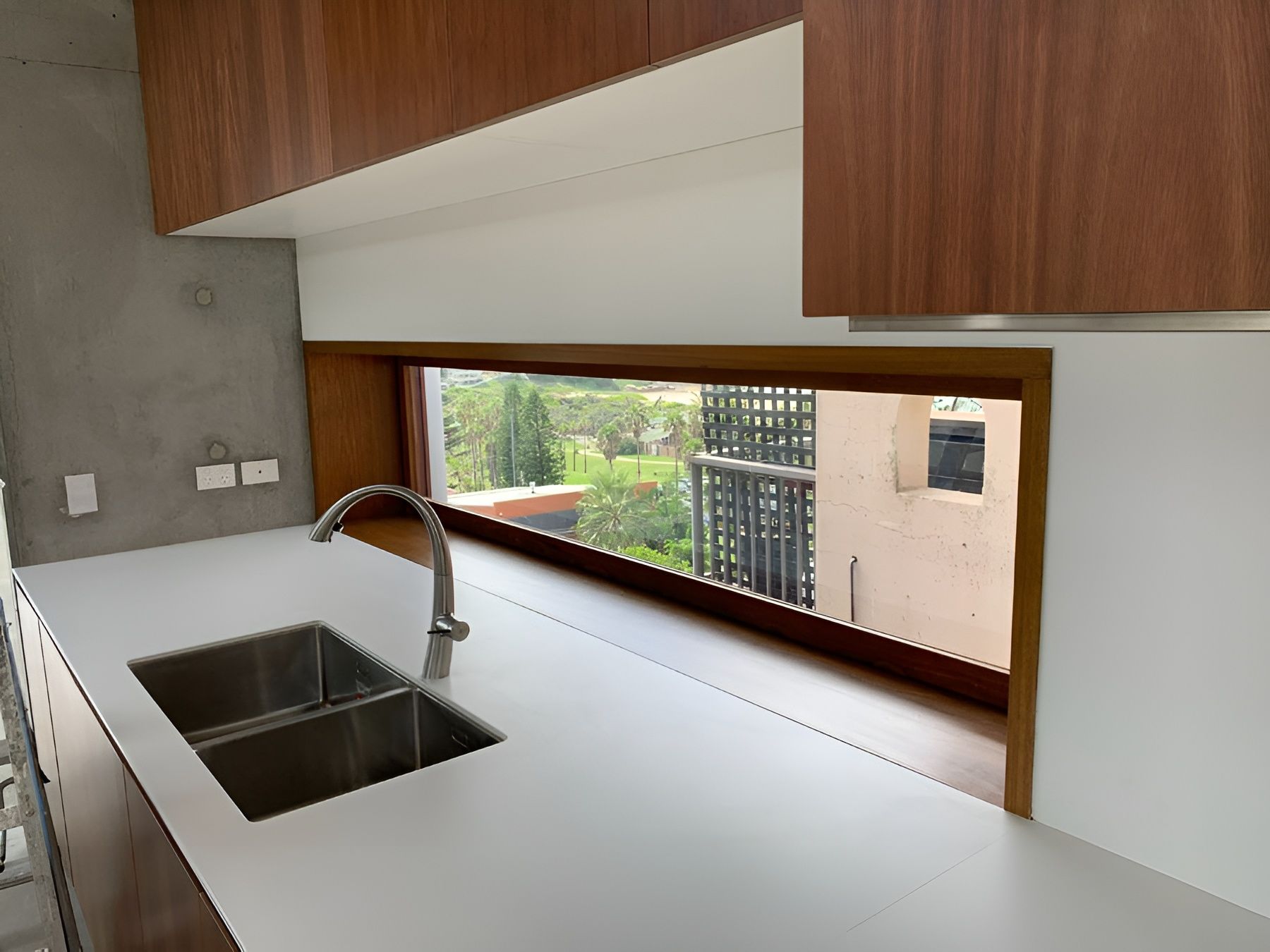 Modern kitchen with white countertop, double sink, chrome faucet, and a wide window opening to greenery. — Fineworx Joinery in Warnervale, NSW