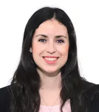 Woman with dark hair smiling at the camera, wearing a black blazer and pink top.
