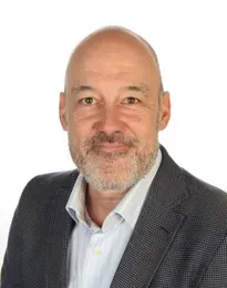 Man with a shaved head and gray beard, wearing a blazer over a light blue shirt, smiling.