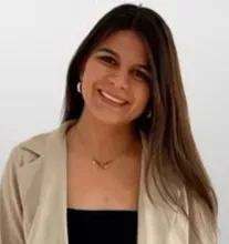 Woman with long brown hair, wearing a tan blazer and black top, smiling at the camera.