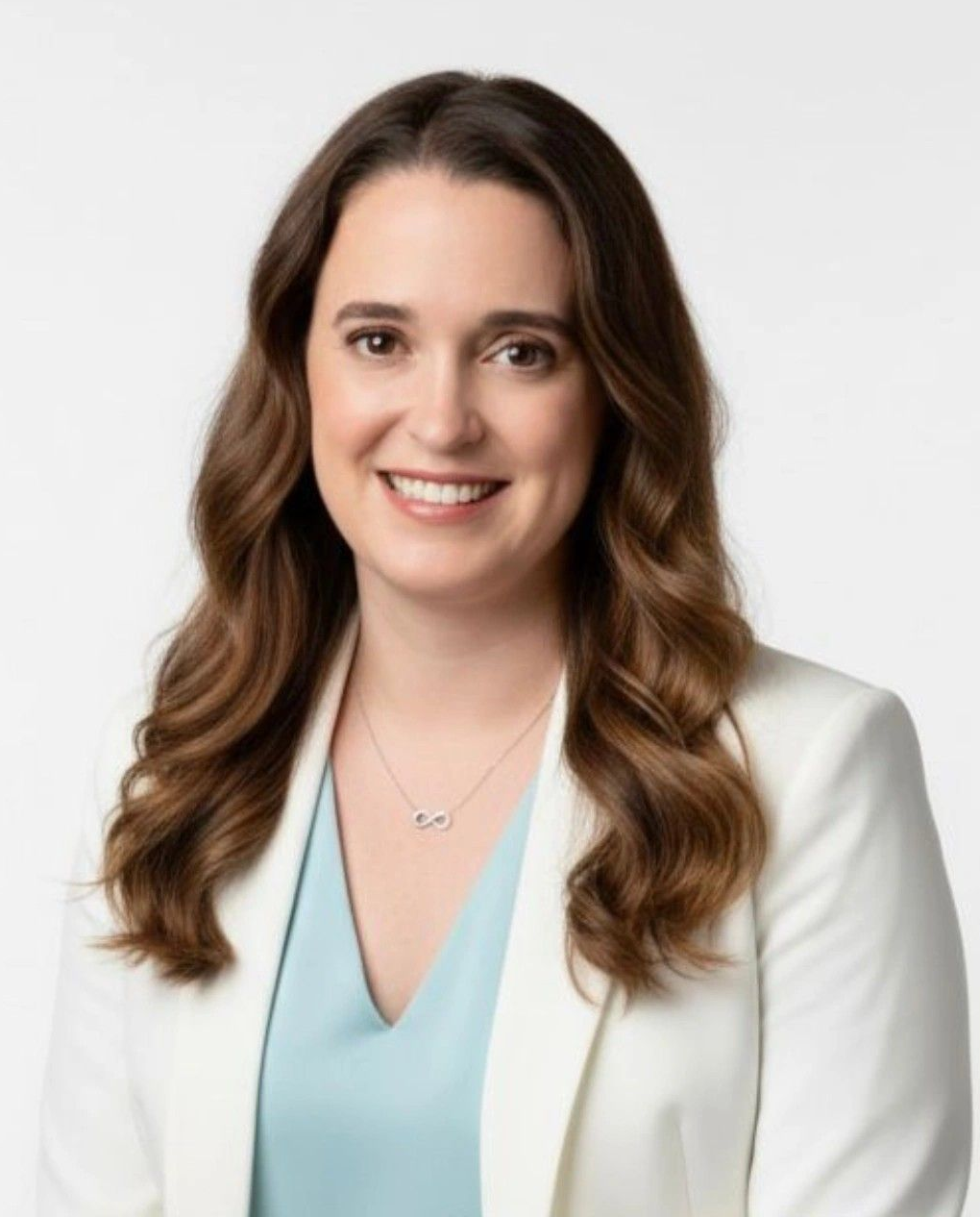 Woman with long brown hair, smiling, wearing a light-colored top, against a white background.