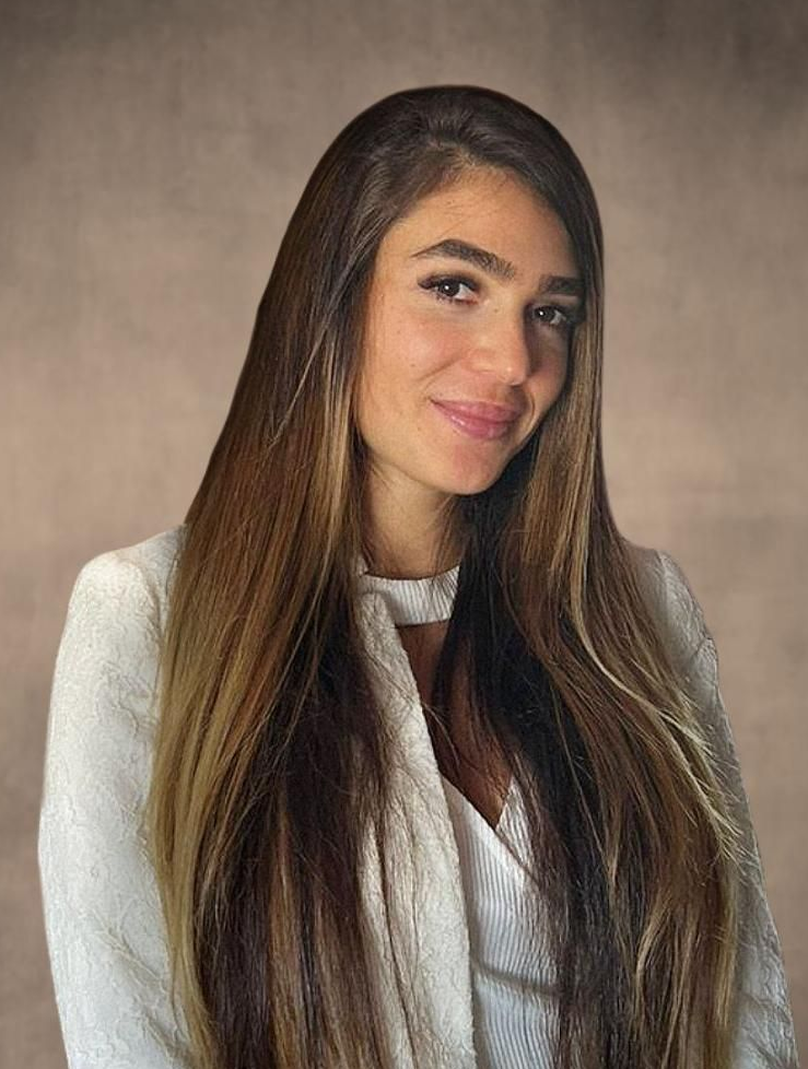 Man in blue sweater, white shirt, smiling outdoors.