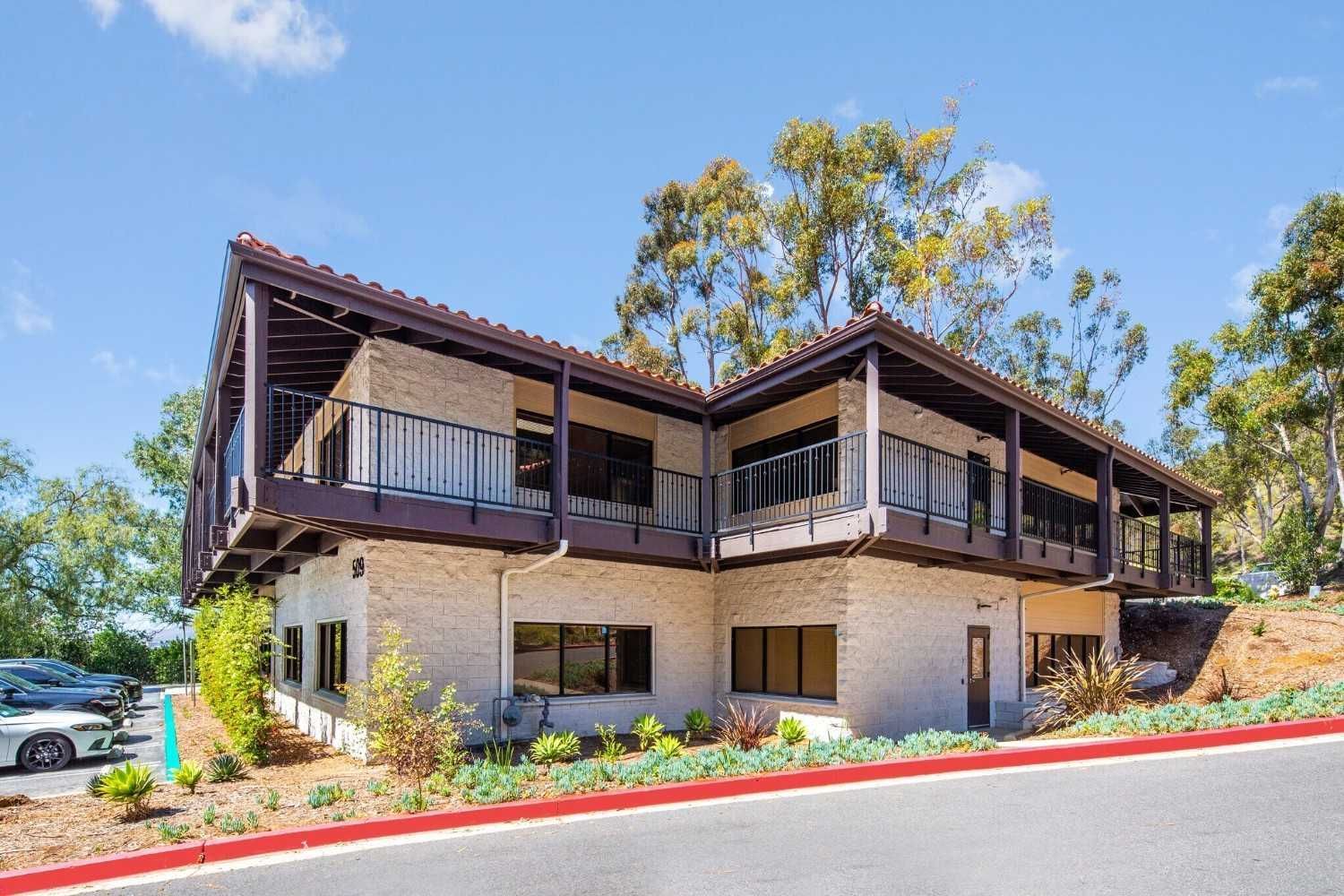 A white car is parked in front of a house with a balcony.