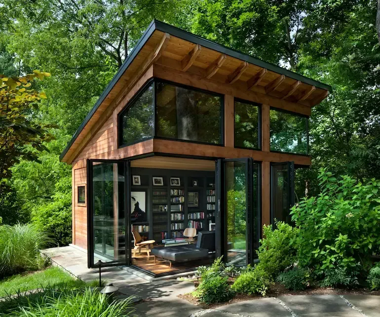 A small house with a lot of windows is surrounded by trees.