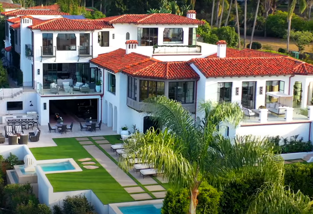 An aerial view of a large white house with a red tile roof surrounded by trees.