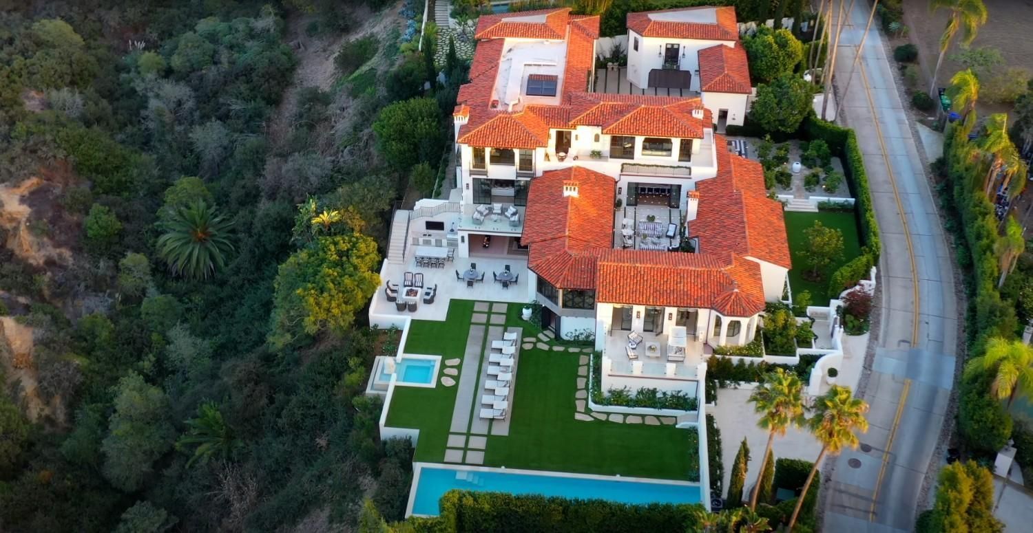 An aerial view of a large house with a swimming pool surrounded by trees.