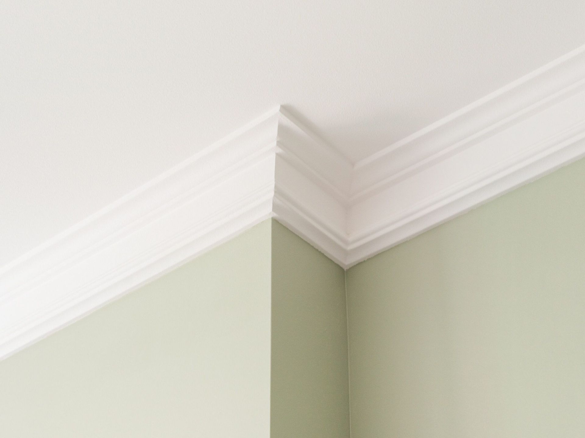 A close up of white crown moulding and a sage wall