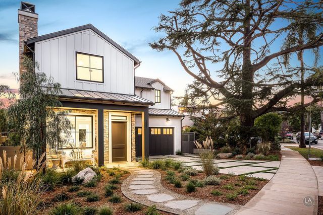 A white house with a black garage door and a tree in front of it