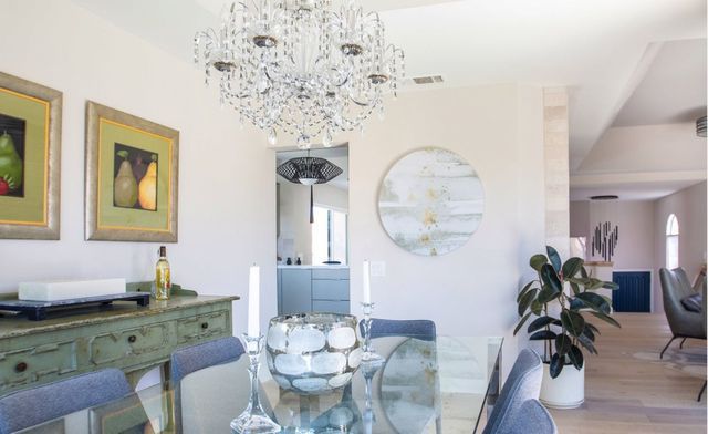 A dining room with a glass table and chairs and a chandelier hanging from the ceiling.