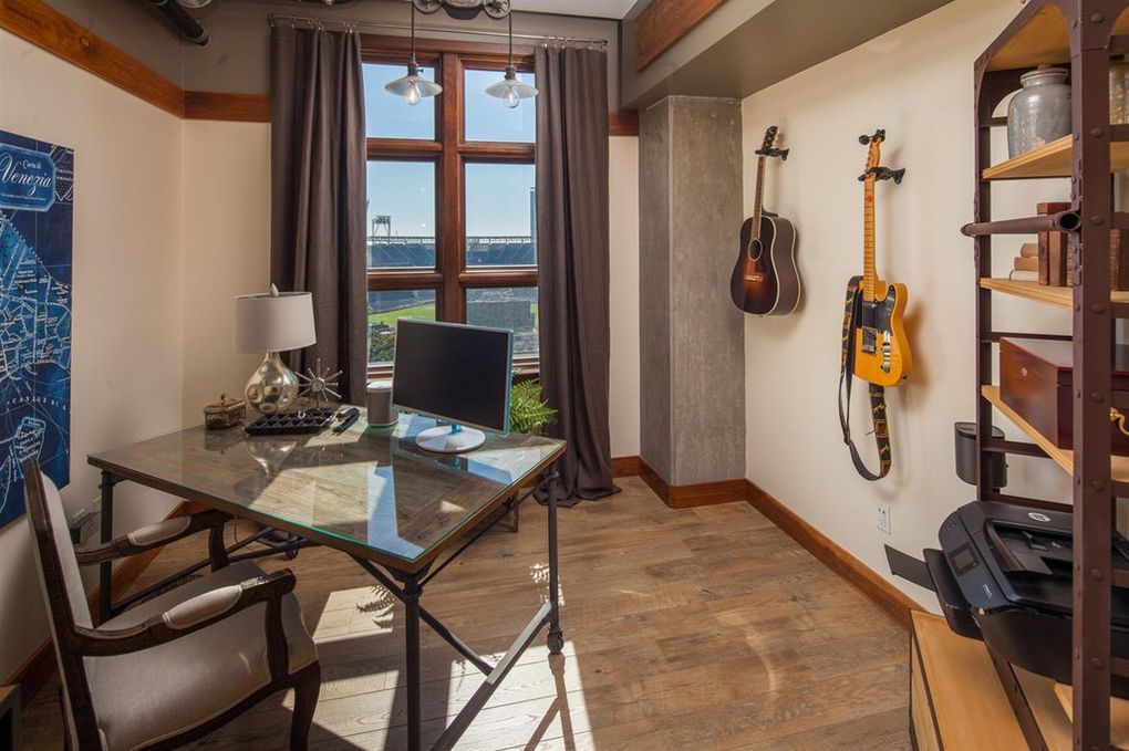 A home office with a desk , chair , computer and a guitar hanging on the wall.