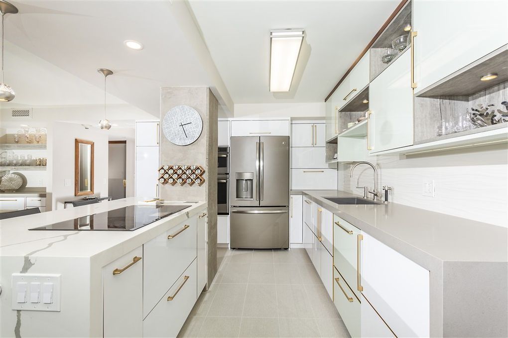 A kitchen with white cabinets , stainless steel appliances and a clock on the wall.